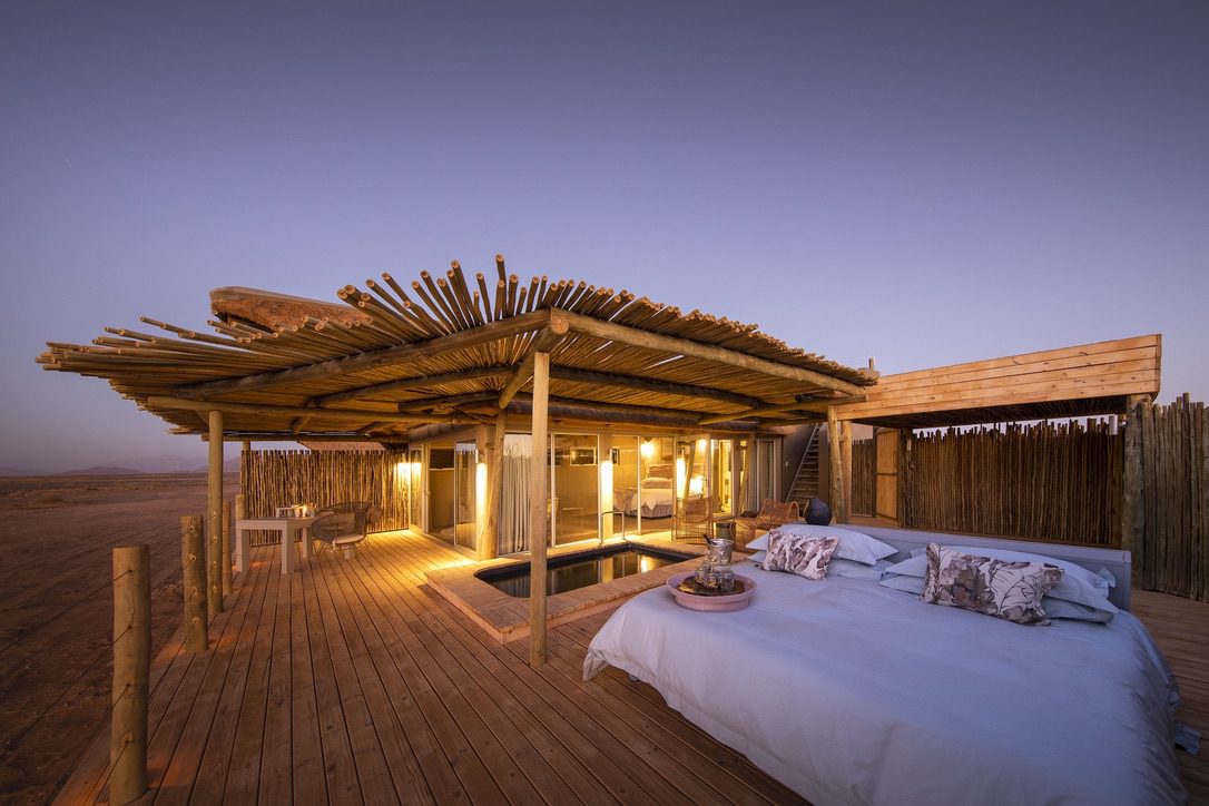 Open air sleeping deck at dusk featuring an open-air bedroom, seating area, plunge pool, and rustic wood canopy.