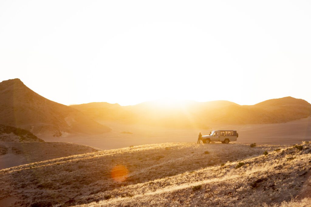 A safari vehicle silhouetted against a backdrop of rolling grassy hills creating a scene of calm exploration.