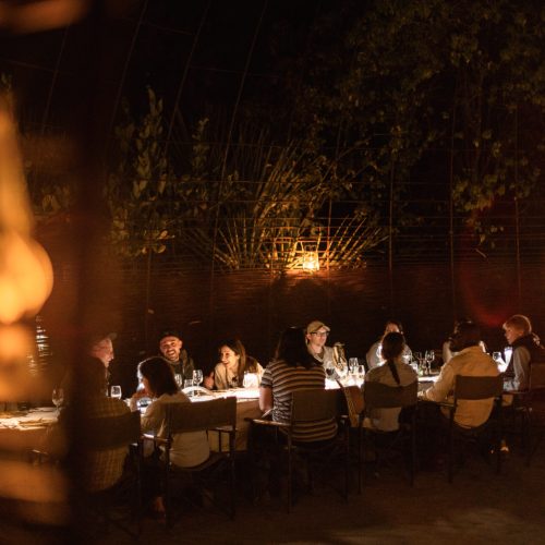 A group of people dining al fresco in the boma of a safari camp, lit by lanterns, evoking a sense of adventure and luxury.